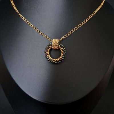 Elegancki naszyjnik ze złotą zawieszką oplataną zielonymi koralikami. Doskonały dodatek zarówno do codziennych, jak i wieczorowych stylizacji. Biżuteria ze stali nierdzewnej o wysokiej trwałości i wyrafinowanym wyglądzie.