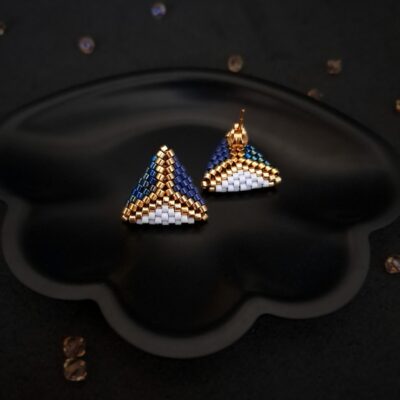 leganckie kolczyki w kształcie trójkąta z niebieskimi i złotymi akcentami – geometryczny wzór dla kobiet ceniących sobie nowoczesny design. Idealne na prezent lub eleganckie wyjścia. Kolczyki na sztyftach w kształcie trójkąta z koralikami Miyuki – ręcznie wykonane, precyzyjnie dobrane odcienie niebieskiego i złota. Elegancka biżuteria na różne okazje.