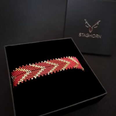 Jesienna czerwona bransoletka o wyrazistym wzorze jodełki, ręcznie wykonana z koralików w odcieniach czerwieni, brązu i złota. Elegancki, luksusowy dodatek dla kobiet ceniących unikatowy styl i precyzyjne wykonanie, idealny na wyjątkowe okazje i do codziennych stylizacji.