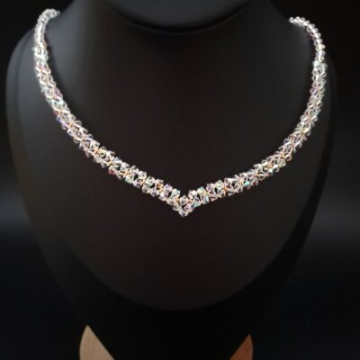 Elegancki złoty naszyjnik ślubny Preciosa Crystal AB na szyi modelki. Kryształki w odcieniu przejrzystego blasku lśnią tęczowymi refleksami, oplecione złotymi koralikami. Ręcznie wykonana biżuteria dla panny młodej, idealna na ślub lub wieczorowe przyjęcie, podkreślająca romantyczny styl.