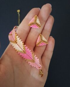 Zestaw Biżuterii Pink Chevron to ręcznie wykonana bransoletka o szerokości 1,5 cm (na nadgarstek 15–16,5 cm) i kolczyki w formie trójkątów 1,5 × 1,5 cm. Oba elementy ze stali nierdzewnej, z odcieniami różu i złota.