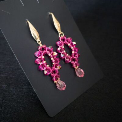 Ręcznie wykonane kolczyki z różowych kryształków Preciosa Bicone Fuchsia i zawieszką Rose, ze złotymi koralikami i złotymi biglami. Kolczyki zachwycają intensywną barwą i błyskiem, dzięki czemu nadają się na prezent oraz do stylizacji eleganckich i casualowych. Biżuteria lekka, trwała i kobieca.