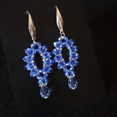 Niebieskie kolczyki wykonane z kryształków Preciosa Sapphire, uzupełnione srebrnymi koralikami i zawieszone na srebrnych biglach. Model wyróżnia się intensywną barwą i błyszczącą kroplą, tworząc elegancki efekt. Idealne do stylizacji eleganckich, koktajlowych i casualowych.