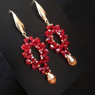 Długie kolczyki handmade z czerwonych kryształków Preciosa Siam, wykończone złotą kroplą Topaz oraz złotymi koralikami i biglami. Model zachwyca intensywnością koloru i mocnym blaskiem, idealnym do stylizacji eleganckich i świątecznych. Kolczyki są lekkie, trwałe i wyraziste.
