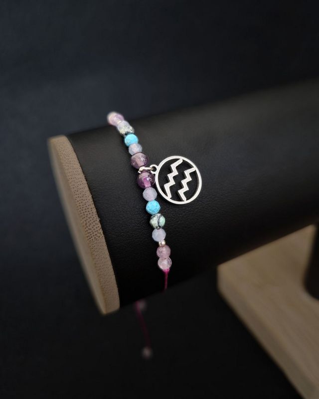 Bransoletka Wodnik wykonana ręcznie z akwamarynu, ametystu i turkusu, na regulowanym fioletowym sznurku makramowym. Zawieszka z symbolem Wodnika nadaje jej indywidualny charakter. Idealna jako prezent urodzinowy lub talizman wolności.