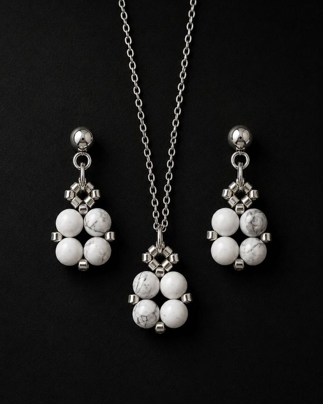 Komplet biżuterii handmade z naturalnym howlitem, obejmujący naszyjnik z zawieszką około 1,5 × 1 cm oraz wiszące kolczyki ze srebrnymi detalami. Howlit jest kamieniem kojarzonym ze spokojem, cierpliwością, wyciszeniem i równowagą emocjonalną.