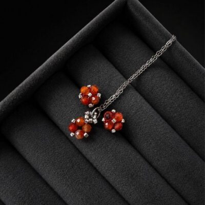 Komplet biżuterii handmade z karneolu obejmujący naszyjnik z zawieszką oraz kolczyki sztyfty. Naturalne pomarańczowe kamienie połączone ze srebrnymi koralikami Miyuki i stalą nierdzewną. Zawieszka o wymiarach około 1,5 × 0,7 cm.