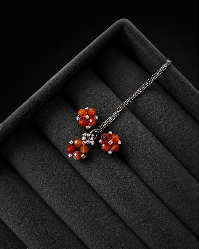 Komplet biżuterii handmade z karneolu obejmujący naszyjnik z zawieszką oraz kolczyki sztyfty. Naturalne pomarańczowe kamienie połączone ze srebrnymi koralikami Miyuki i stalą nierdzewną. Zawieszka o wymiarach około 1,5 × 0,7 cm.
