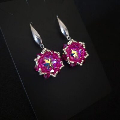Różowe wiszące kolczyki z kryształami Preciosa Fuchsia AB i centralnymi Rivoli Maxima Crystal AB 12 mm. Ręcznie wyplatane kolczyki długości około 4 cm zdobią srebrne koraliki Miyuki i elementy ze stali chirurgicznej.