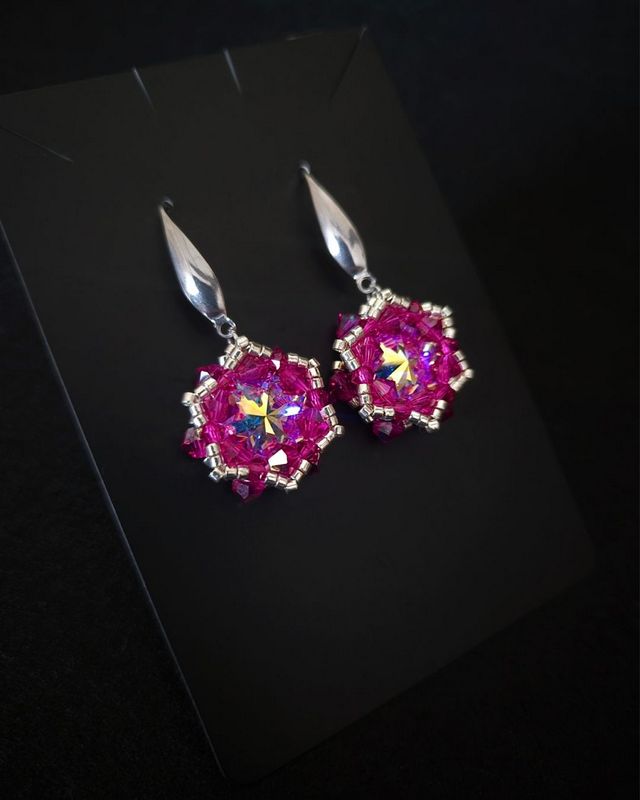 Różowe wiszące kolczyki z kryształami Preciosa Fuchsia AB i centralnymi Rivoli Maxima Crystal AB 12 mm. Ręcznie wyplatane kolczyki długości około 4 cm zdobią srebrne koraliki Miyuki i elementy ze stali chirurgicznej.