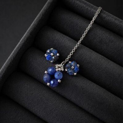Komplet biżuterii handmade z lapis lazuli obejmujący srebrny naszyjnik z zawieszką oraz kolczyki sztyfty. Naturalne granatowe kamienie połączone ze srebrnymi koralikami Miyuki i stalą nierdzewną. Zawieszka o wymiarach około 1,5 × 1 cm.