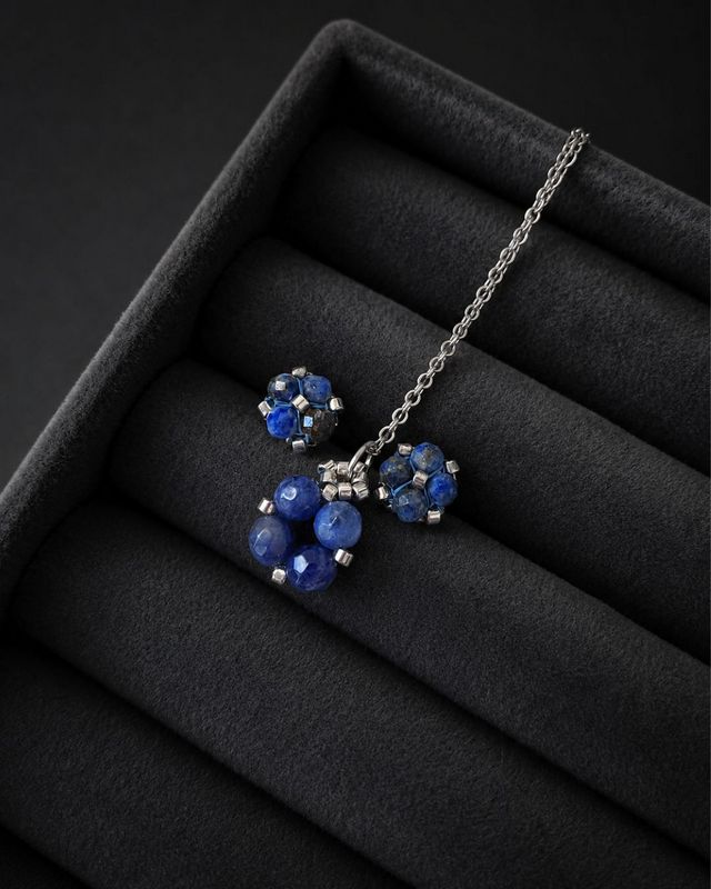 Komplet biżuterii handmade z lapis lazuli obejmujący srebrny naszyjnik z zawieszką oraz kolczyki sztyfty. Naturalne granatowe kamienie połączone ze srebrnymi koralikami Miyuki i stalą nierdzewną. Zawieszka o wymiarach około 1,5 × 1 cm.
