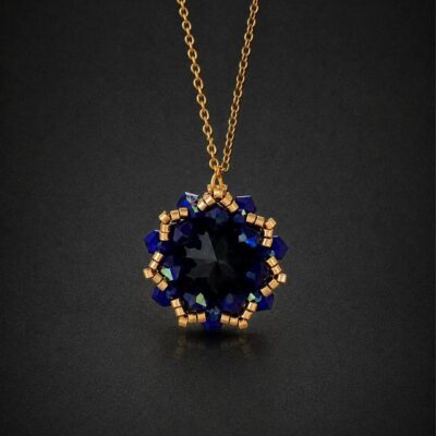Elegancki złoty naszyjnik na wesele Cobalt Maxima z czarnym kryształem Preciosa Rivoli Maxima Jet i kobaltowymi kryształkami Bicone Cobalt AB. Ręcznie wykonana zawieszka około 2,7 × 2,9 cm z opalizującymi refleksami błękitu i fioletu na łańcuszku ze stali nierdzewnej.