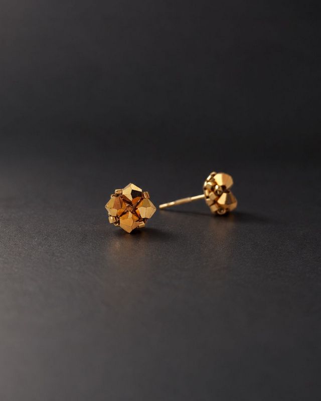 Minimalistyczne złote kolczyki sztyfty z kryształami Preciosa Crystal Aurum o lustrzanym, metalicznym wykończeniu. Ręcznie wyplatane kryształki Bicone 4 mm ze złotymi koralikami Miyuki Delica tworzą niewielkie kolczyki ze stali nierdzewnej o średnicy około 7 mm.